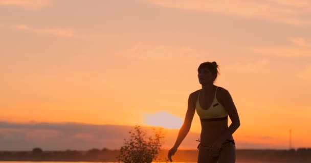 Pomalý pohyb, nízký úhel, zavřít, sluneční erupce: atletická dívka hrající na plážový volejbal ve vzduchu a udeří míč přes síť za krásný letní večer. Ta Kavkazská žena bodne — Stock video