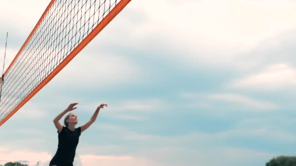 Mladá žena hrající volejbal na pláži v týmu, který provádí útok na míč. Dívka v pomalém pohybu zasáhne míč a provede útok sítí