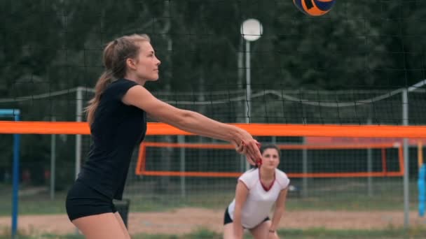 Mujer joven jugando voleibol en la playa en un equipo llevando a cabo un ataque golpeando la pelota. Chica en cámara lenta golpea la pelota y llevar a cabo un ataque a través de la red — Vídeo de stock