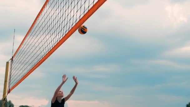 Giovane donna che gioca a pallavolo sulla spiaggia in una squadra che effettua un attacco che colpisce la palla. Ragazza al rallentatore colpisce la palla ed effettuare un attacco attraverso la rete — Video Stock