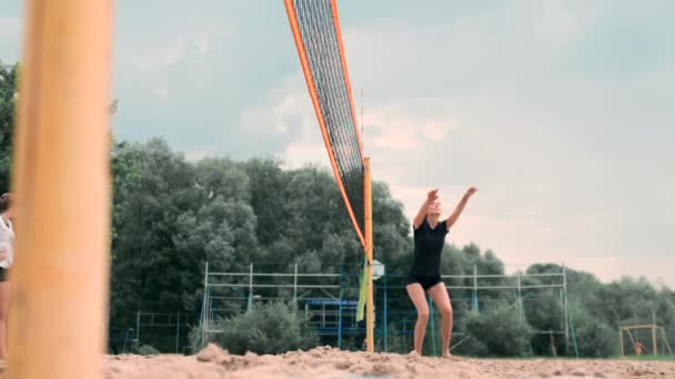 Mujer joven jugando voleibol en la playa en un equipo llevando a cabo un ataque golpeando la pelota. Chica en cámara lenta golpea la pelota y llevar a cabo un ataque a través de la red — Vídeos de Stock