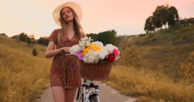 Parkta retro bisiklete binen ve kameraya bakan elbise ve şapkalı mutlu kız gülümseyen