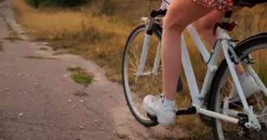 Parkta retro bisiklete binen ve kameraya bakan elbise ve şapkalı mutlu kız gülümseyen