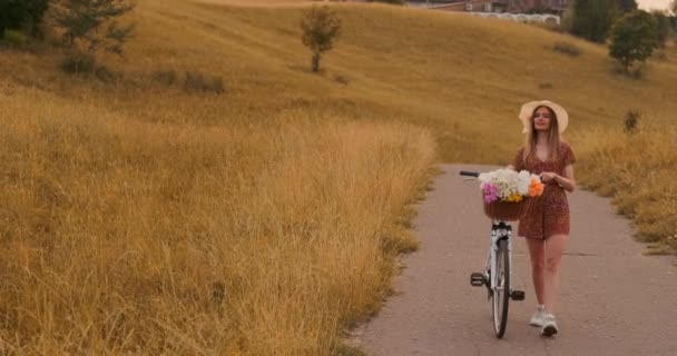 Piękna kobieta z rowerem w kapeluszu i lekka Letnia sukienka pochodzi z kwiatów w koszyku i uśmiechy. — Wideo stockowe