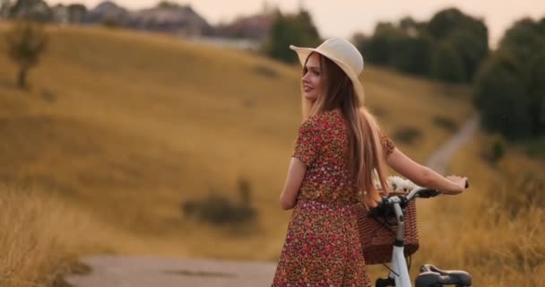 Девушка в шляпе с велосипедом поворачивается и смотрит в камеру улыбаясь . — стоковое видео