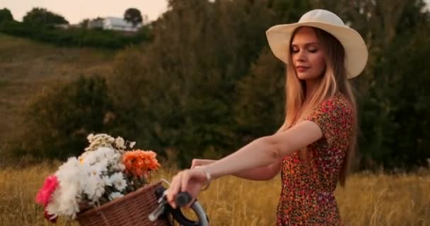 Şapka ve elbise sepette bisiklet ve çiçekler ile elbise yürüyüş genç gülümseyen sarışın. — Stok video
