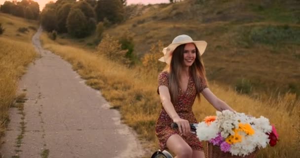 Šťastná dívka s kyticí květinami na kole v klobouku a v letních krátkých šatech. — Stock video