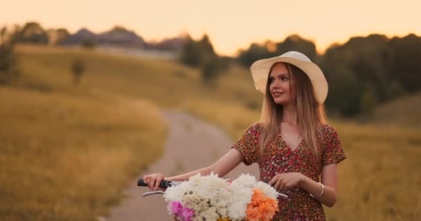 Porter meisje wandelen op de camera in een jurk met bloemen in een mand en een fiets in het veld. — Stockvideo