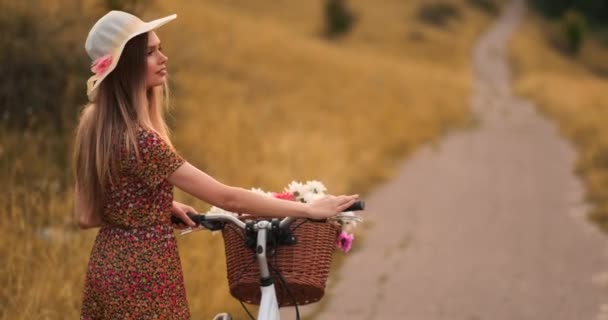 Uśmiechnięta szczęśliwa dziewczyna w sukni i kapelusz jazdy retro rower w parku i patrząc na kamerę — Wideo stockowe