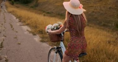 Bir şapka ve bir yaz kısa elbise bir bisiklet sürme çiçek bir buket ile Mutlu kız.