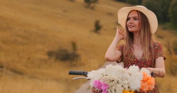 Porter meisje wandelen op de camera in een jurk met bloemen in een mand en een fiets in het veld. — Stockvideo