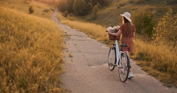 Une fille dans un chapeau avec un vélo se retourne et regarde la caméra sourire . — Video