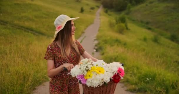 Porter meisje wandelen op de camera in een jurk met bloemen in een mand en een fiets in het veld. — Stockvideo