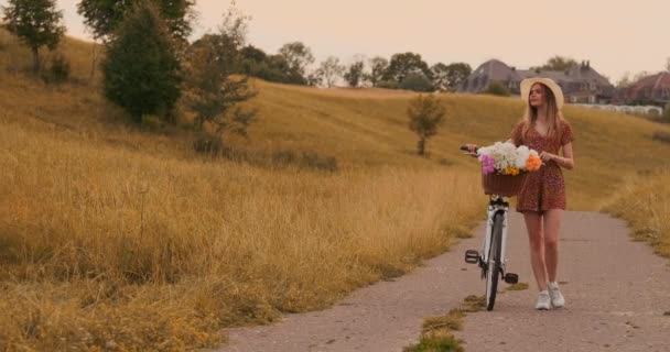 Χαμογελαστά ευτυχισμένο κορίτσι σε φόρεμα και καπέλο ιππασία ρετρό ποδήλατο στο πάρκο και κοιτάζοντας την κάμερα — Αρχείο Βίντεο