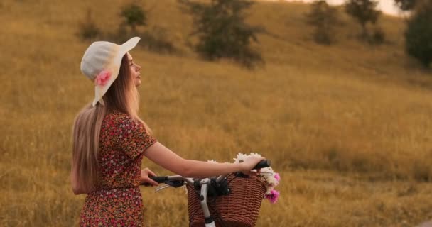 Geri plan: Elbise ve retro bisiklet yaz alanında yolda yürüyen güzel sarışın. — Stok video