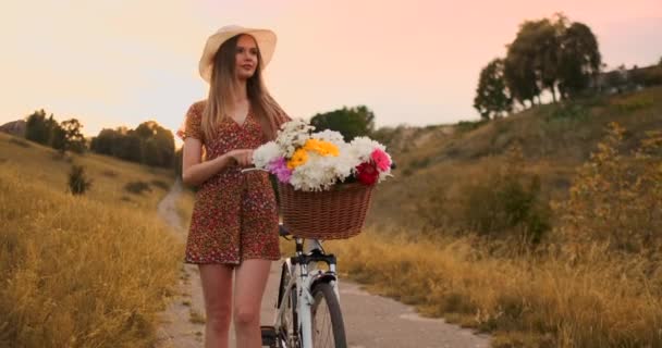 Środkowy plan dziewczyna w sukni idzie z rowerem i kwiatami w terenie. — Wideo stockowe