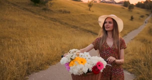 Środkowy plan dziewczyna w sukni idzie z rowerem i kwiatami w terenie. — Wideo stockowe