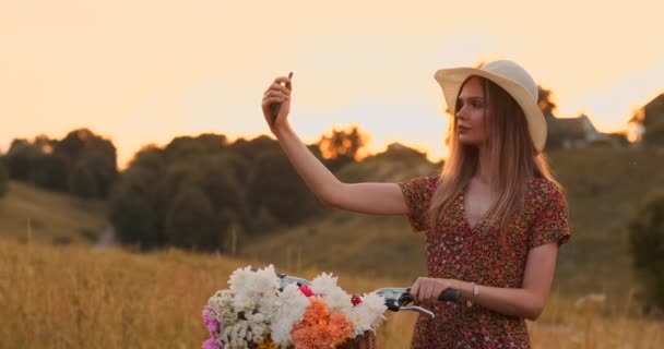 Meisje met een fiets in een hoed maakt een selfie met behulp van een smartphone. — Stockvideo