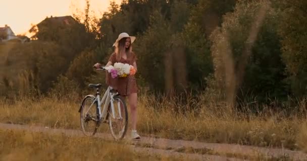 Zomer in het veld meisje met bloemen en een hoed gaat met een fiets op de weg — Stockvideo