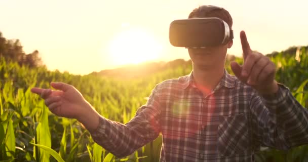 Agricultor masculino em óculos de realidade virtual no campo ao pôr do sol controla o sistema de irrigação de milho — Vídeo de Stock