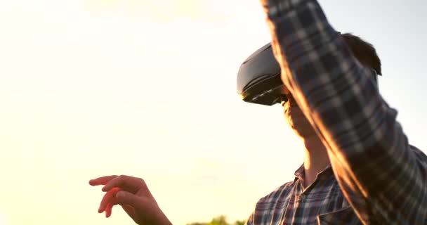 Homme agriculteur en réalité virtuelle lunettes dans le champ au coucher du soleil contrôle le système d'irrigation du maïs — Video