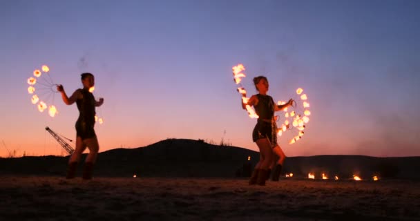 プロのアーティストは、スローモーションで砂の上の夏祭りで火のショーを示しています。ビーチで夜に火でサーカスの仕事から4人目のアクロバット. — ストック動画