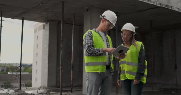 Два інженери чоловік і жінка з планшетним комп'ютером на будівельному майданчику засуджують план будівництва будівлі — стокове відео
