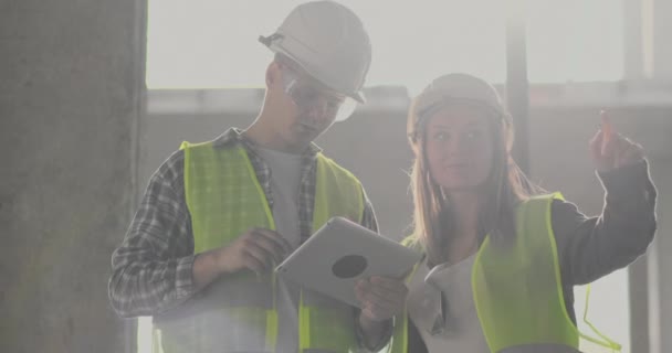 Budowy pracownik człowieka i architekt Kobieta w kasku, omówić plan budowy domu, powiedzieć sobie nawzajem o projektowanie, trzymając tablet, patrzeć na rysunki, tło promieni słonecznych — Wideo stockowe