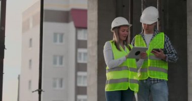 İnşaat işçisi adam ve mimar kadın bir kask içinde evin inşaat planını tartışmak, diğer her bir tablet tutan tasarımı hakkında söyle, çizimler, güneş ışınlarının arka plan bakmak