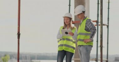 İki mühendis bir adam ve bir inşaat yerinde tablet bilgisayar ile bir kadın binanın inşaat planını kınaz
