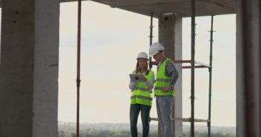 İnşaat sitesi takım veya mimar ve kurucu veya işçi kask ile bir iskele inşaat planı veya plan veya kontrol listesi üzerinde tartışmak.