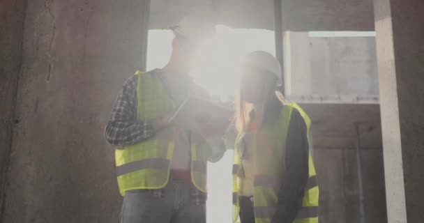 Dos ingenieros un hombre y una mujer con una tableta en un sitio de construcción condenan el plan de construcción del edificio — Vídeo de stock