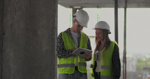 Два инженера мужчина и женщина с планшетным компьютером на строительной площадке осуждают план строительства здания — стоковое видео