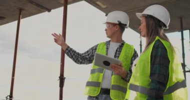 İnşaat işçisi adam ve mimar kadın bir kask içinde evin inşaat planını tartışmak, diğer her bir tablet tutan tasarımı hakkında söyle, çizimler, güneş ışınlarının arka plan bakmak