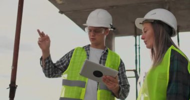 İnşaat sitesi takım veya mimar ve kurucu veya işçi kask ile bir iskele inşaat planı veya plan veya kontrol listesi üzerinde tartışmak.