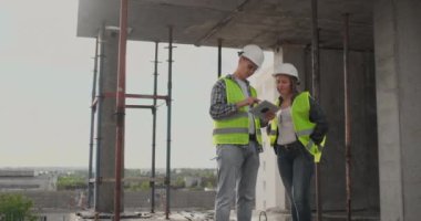 İnşaat sitesi takım veya mimar ve kurucu veya işçi kask ile bir iskele inşaat planı veya plan veya kontrol listesi üzerinde tartışmak.