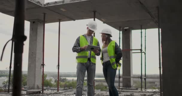 Dua insinyur, seorang pria dan seorang wanita dengan komputer tablet di lokasi konstruksi mengutuk rencana pembangunan gedung — Stok Video