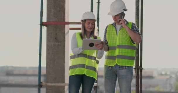 O controlador é um homem de um edifício em construção conversando ao telefone com a gestão e discutiu com o engenheiro e arquiteto progresso da construção da mulher — Vídeo de Stock