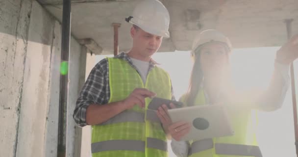 Edificio in costruzione con una femmina e un maschio costruttori, costruttori, ingegneri a piedi lungo di esso . — Video Stock