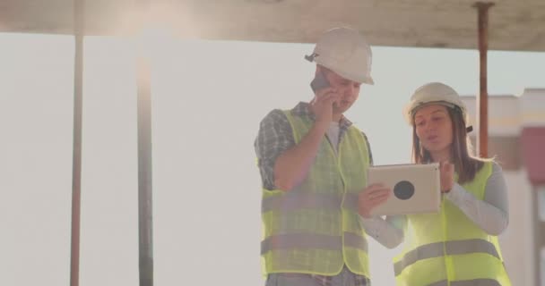 Контроллер - человек строящегося здания, разговаривающий по телефону с руководством и обсудивший с инженером и архитектором прогресс строительства — стоковое видео