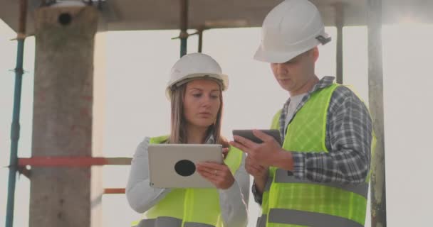 Superviseur d'un bâtiment en construction homme discuter avec l'ingénieur designer femme de l'état d'avancement de la construction et examine un plan de construction — Video