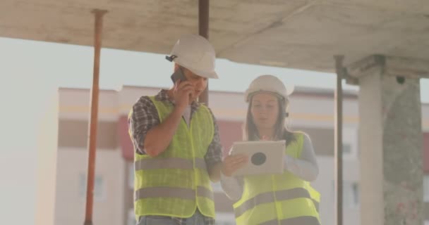 Supervisor de um edifício em construção homem discutindo com engenheiro designer mulher o progresso da construção e examina um plano de construção — Vídeo de Stock