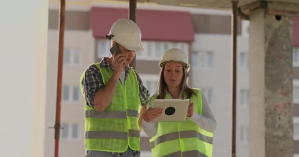 Supervisor de um edifício em construção homem discutindo com engenheiro designer mulher o progresso da construção e examina um plano de construção — Vídeo de Stock