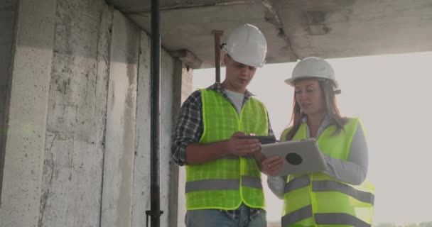 Les ingénieurs concepteurs se tiennent sur le toit du bâtiment en construction et discutent du plan et de l'avancement de la construction à l'aide d'une tablette et d'un téléphone portable — Video