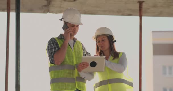 Edificio en construcción con una mujer y un hombre constructores, constructores, ingenieros caminando a lo largo de ella . — Vídeos de Stock