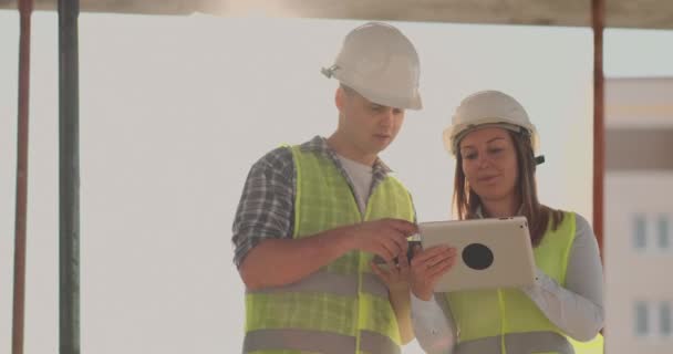 Edificio en construcción con una mujer y un hombre constructores, constructores, ingenieros caminando a lo largo de ella . — Vídeos de Stock