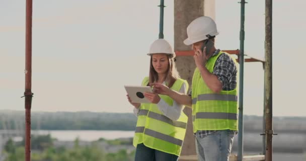 Construção em construção com uma mulher e um homem engenheiros usando um tablet e telefone celular para visualizar o plano de construção . — Vídeo de Stock