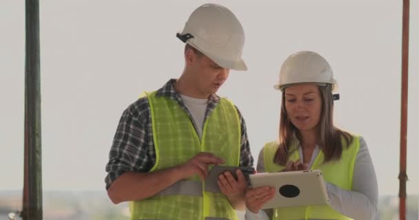 Supervisor de un edificio en construcción hombre discutir con la mujer de diseño ingeniero el progreso de la construcción y examina un plan de construcción — Vídeos de Stock
