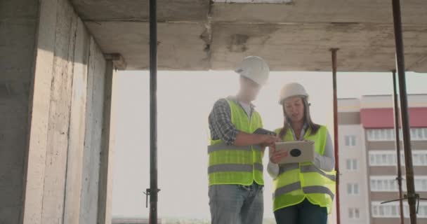 Edificio in costruzione con una donna e un ingegnere di sesso maschile utilizzando un tablet e un telefono cellulare per visualizzare il piano di costruzione . — Video Stock