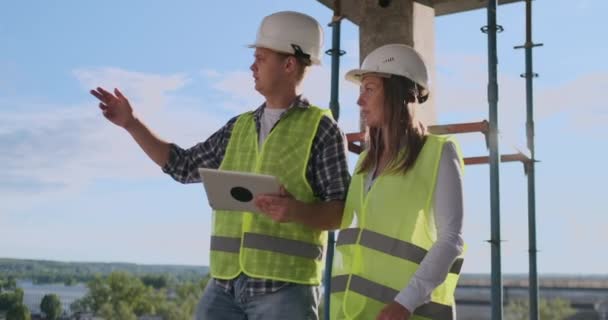 Tecnologia de construção e conceito de pessoas - construtores sorridentes em hardhats com computador tablet pc ao ar livre . — Vídeo de Stock